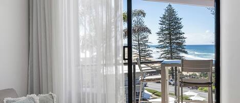 A balcony with a view of the ocean and trees, a chair, and a table.