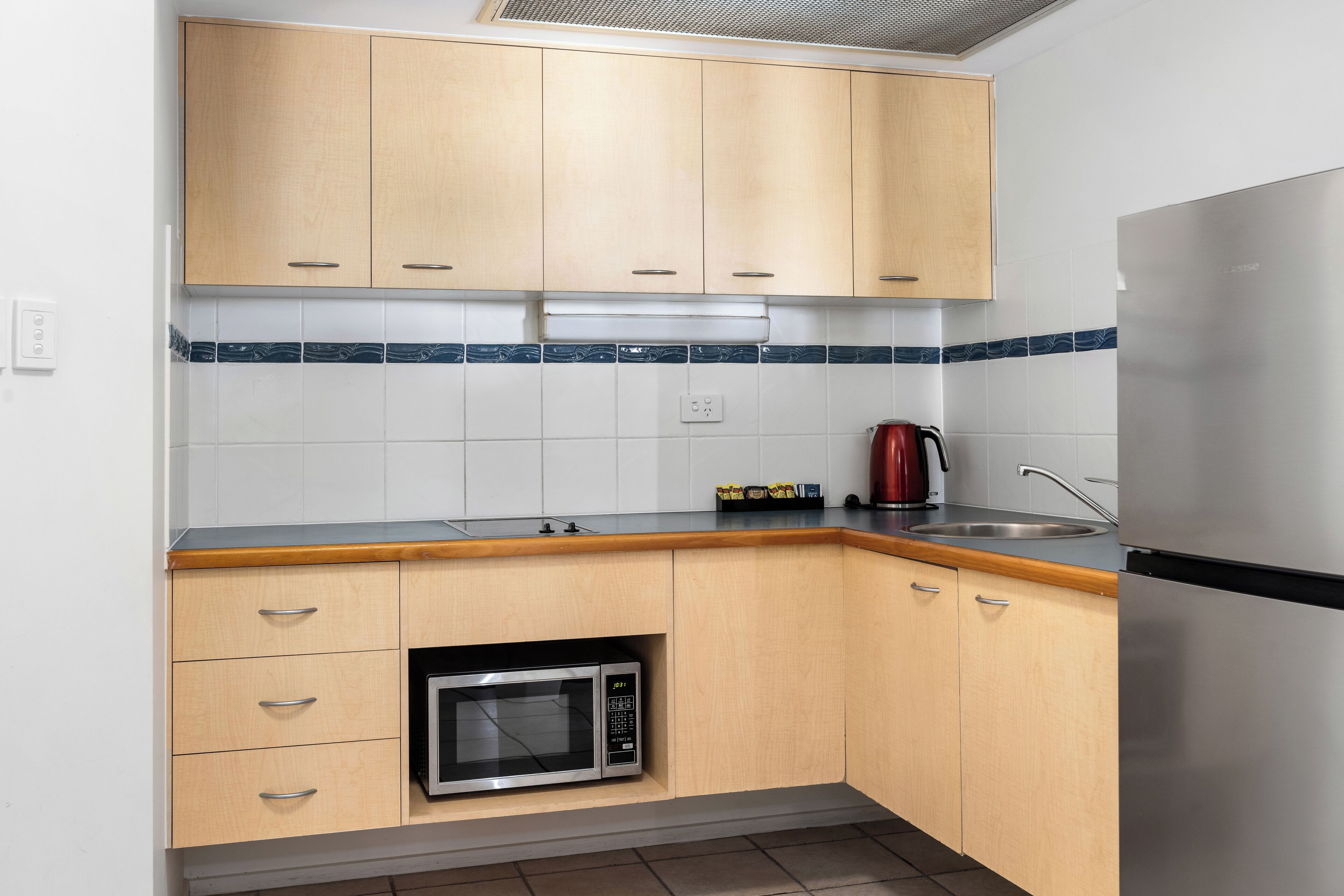 A kitchen with wooden cabinets, a built-in microwave, a stainless steel sink, and a red kettle.