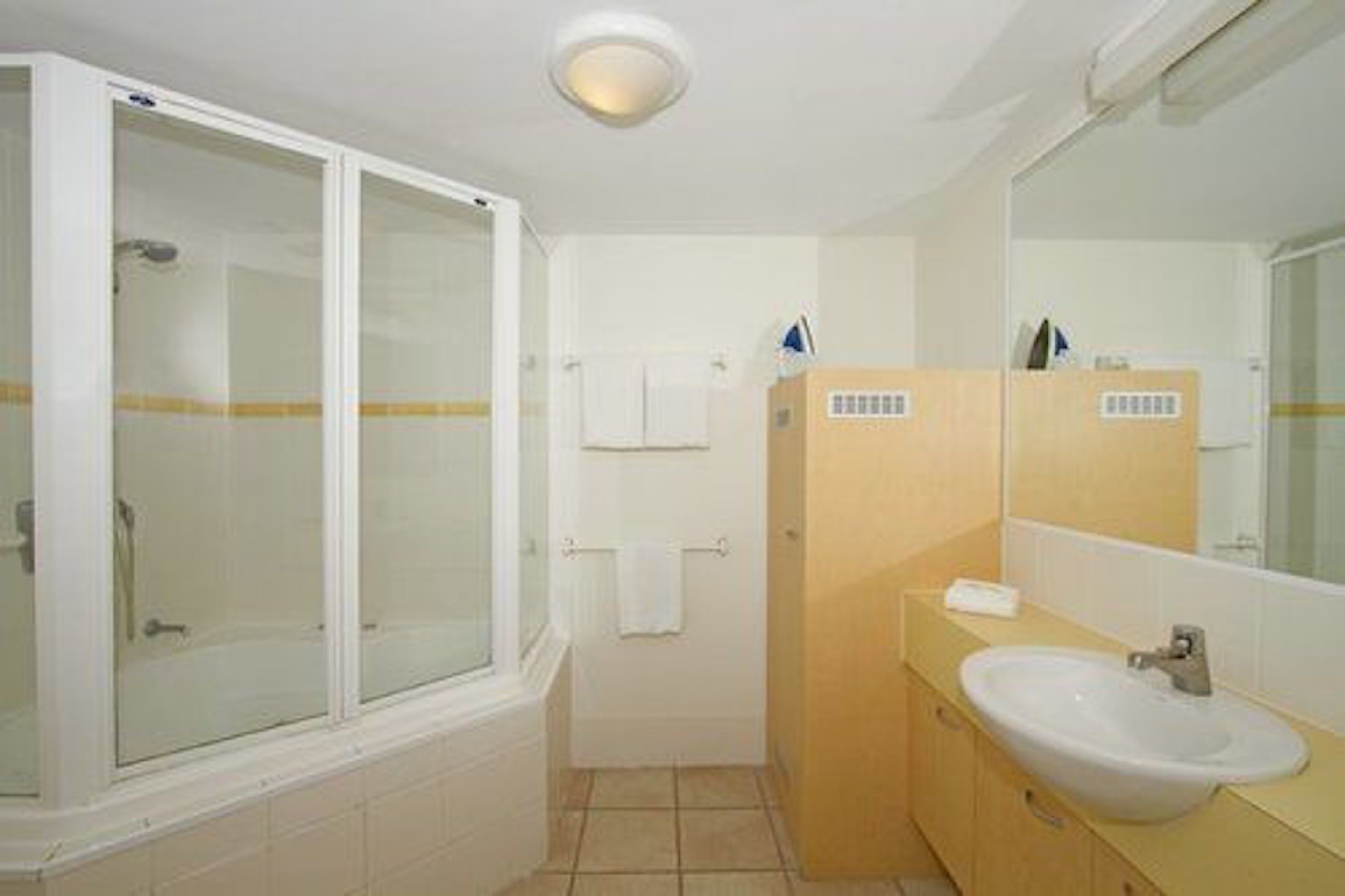Un baño con ducha de vidrio, lavamanos, espejo y toallero.
