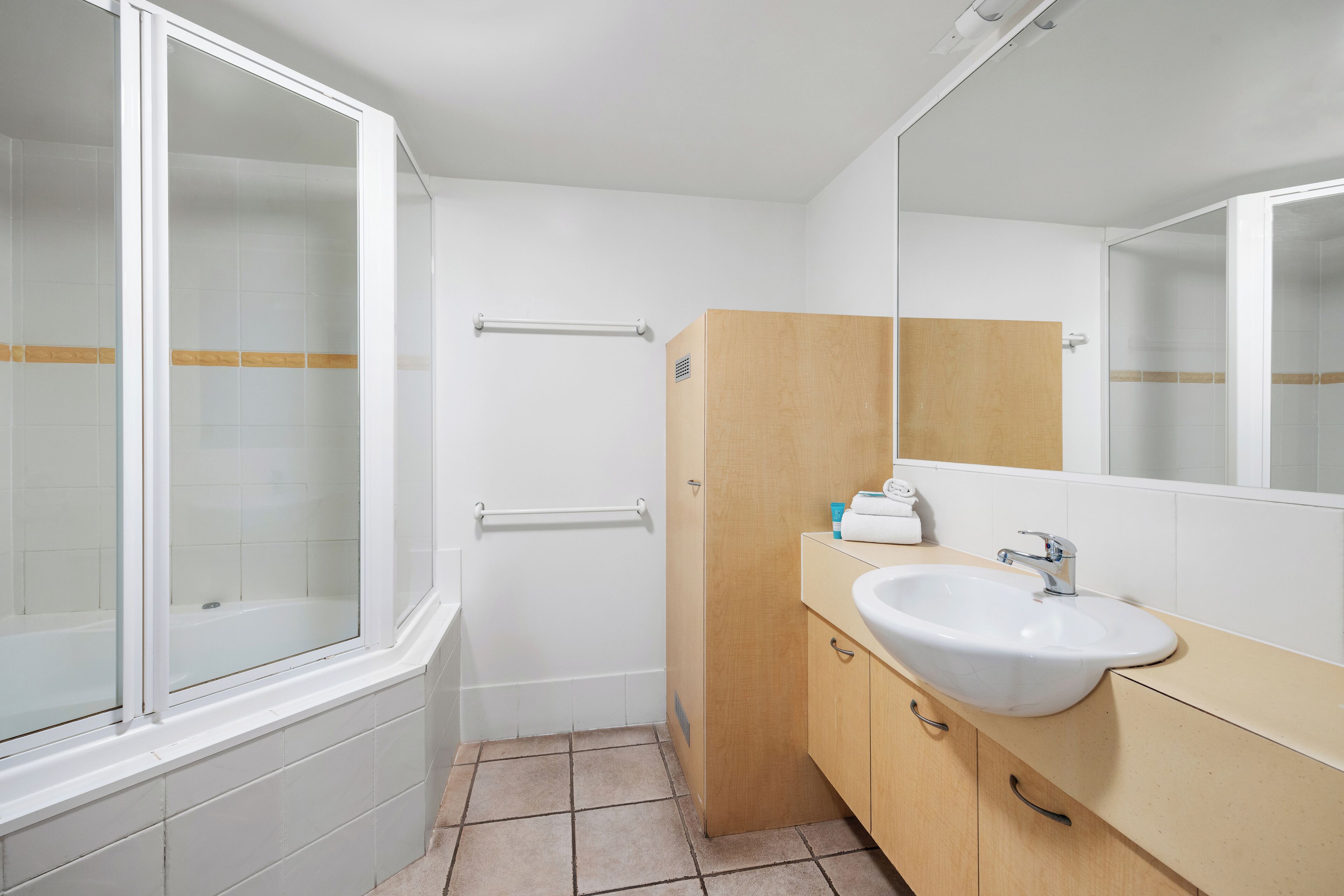 A bathroom with a bathtub, a sink, a mirror, and a wooden cabinet.