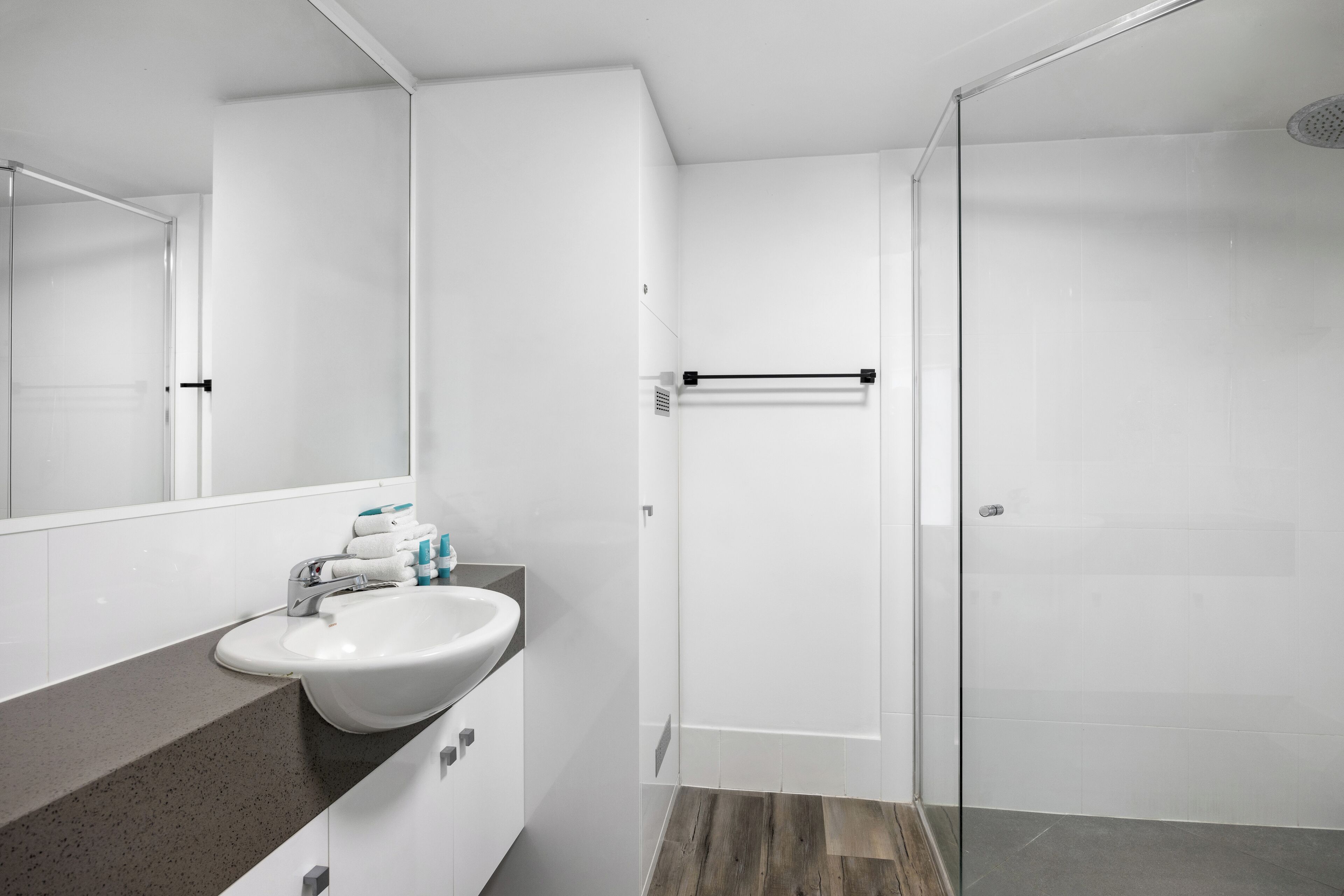 A modern bathroom with a white sink, mirror, and glass shower enclosure.