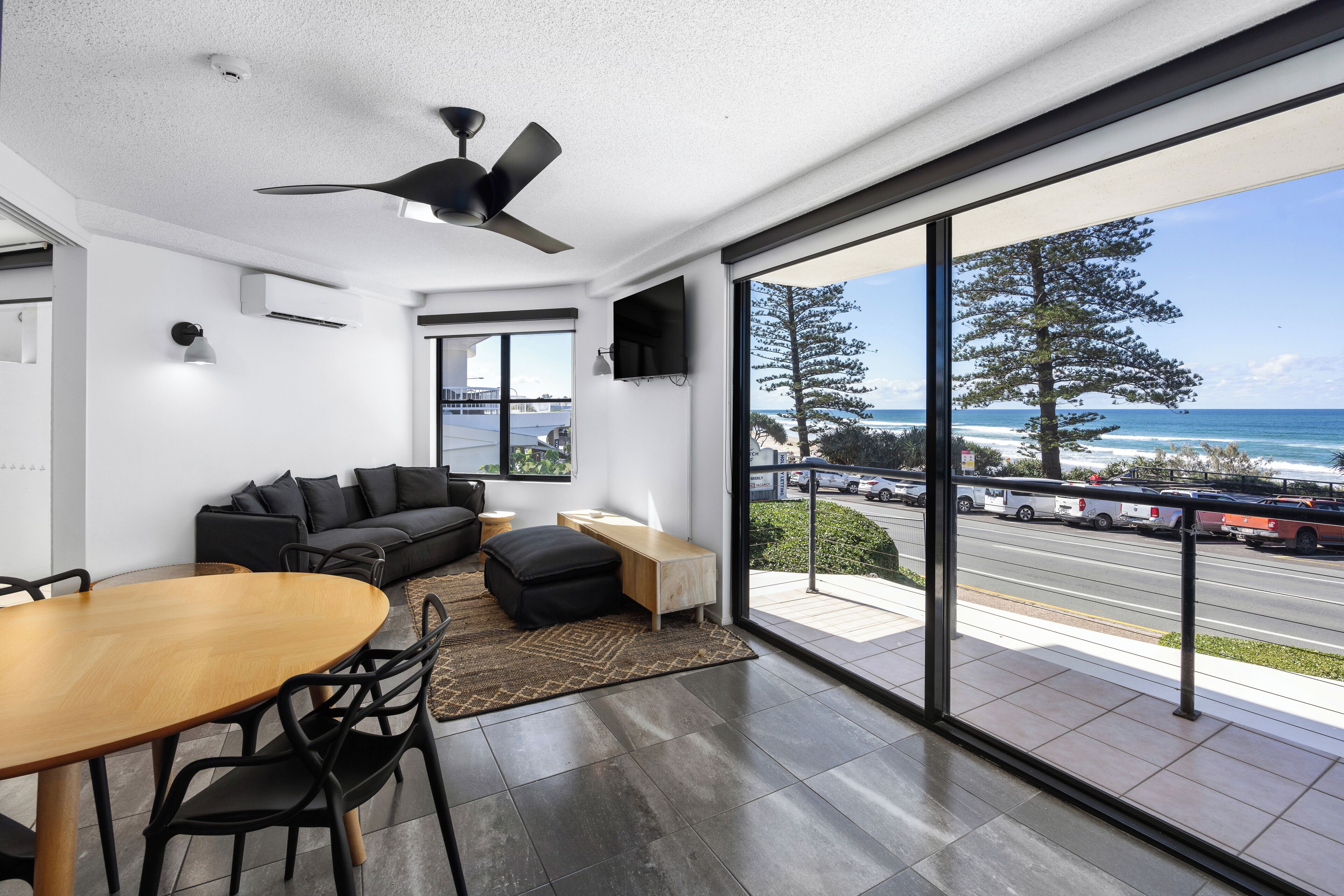 A modern living room with a view of the ocean, a ceiling fan, and a dining area.