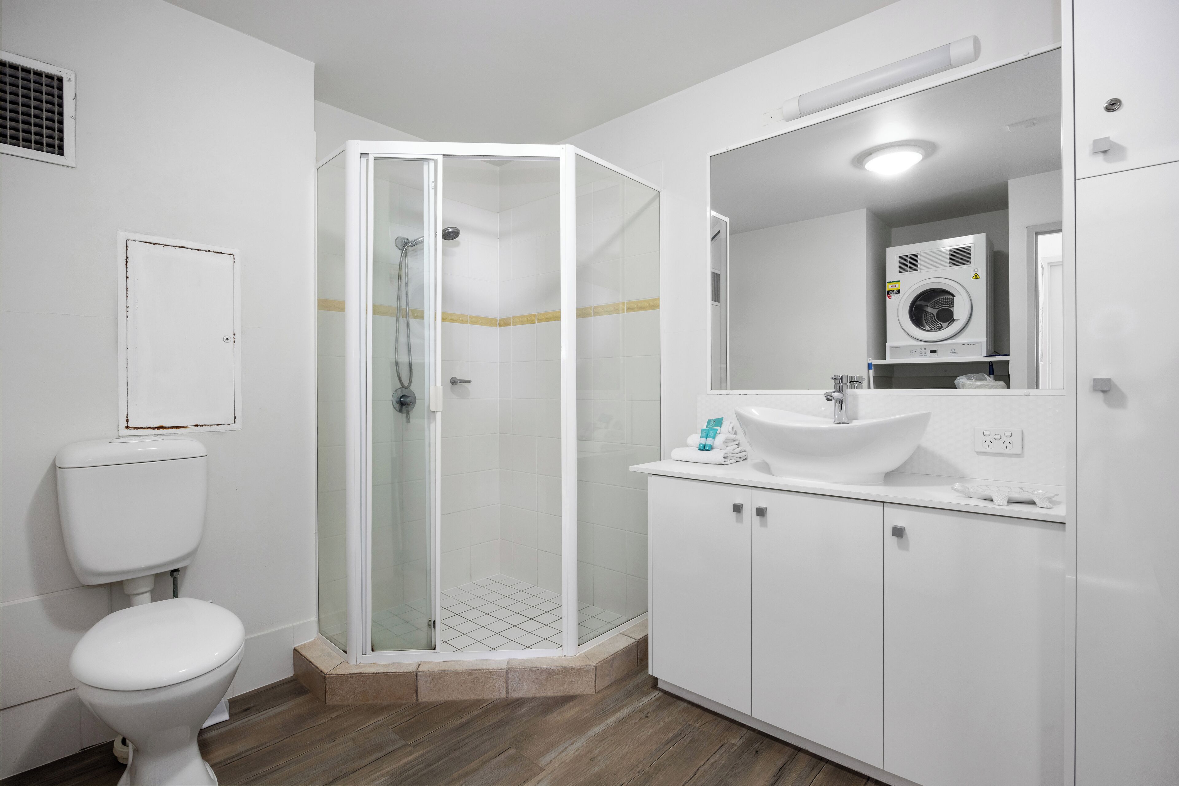 A bathroom with a glass-enclosed shower, a white toilet, a sink with a mirror, and a washing machine.
