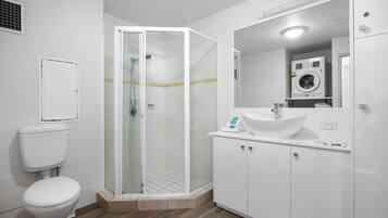 A bathroom with a glass-enclosed shower, a white toilet, a sink with a mirror, and a washing machine.
