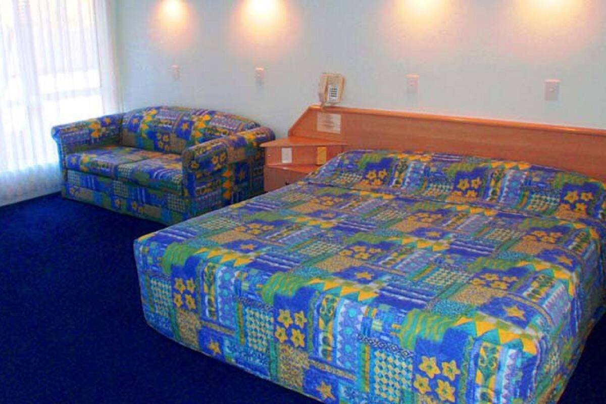 Una habitación de hotel con una cama grande, dos sillones, una mesita de noche de madera y una planta en maceta.