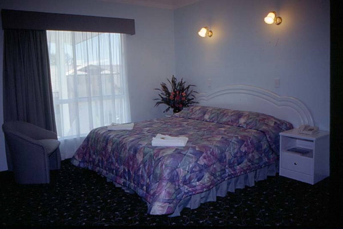 Una habitación de hotel con cama, una silla, una mesita de noche y una ventana con cortinas.