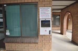 A self-check-in kiosk with instructions for existing and new bookings, a 24-hour check-in option, and a security system notice. - Keith Motor Inn (Keith)