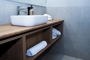 Un baño con un lavabo blanco tipo recipiente, repisas de madera y un perchero para toallas.