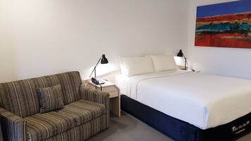 Een hotelkamer met een bed, een gestreept sofa, een nachtkastje met een lamp en een schilderij aan de muur.