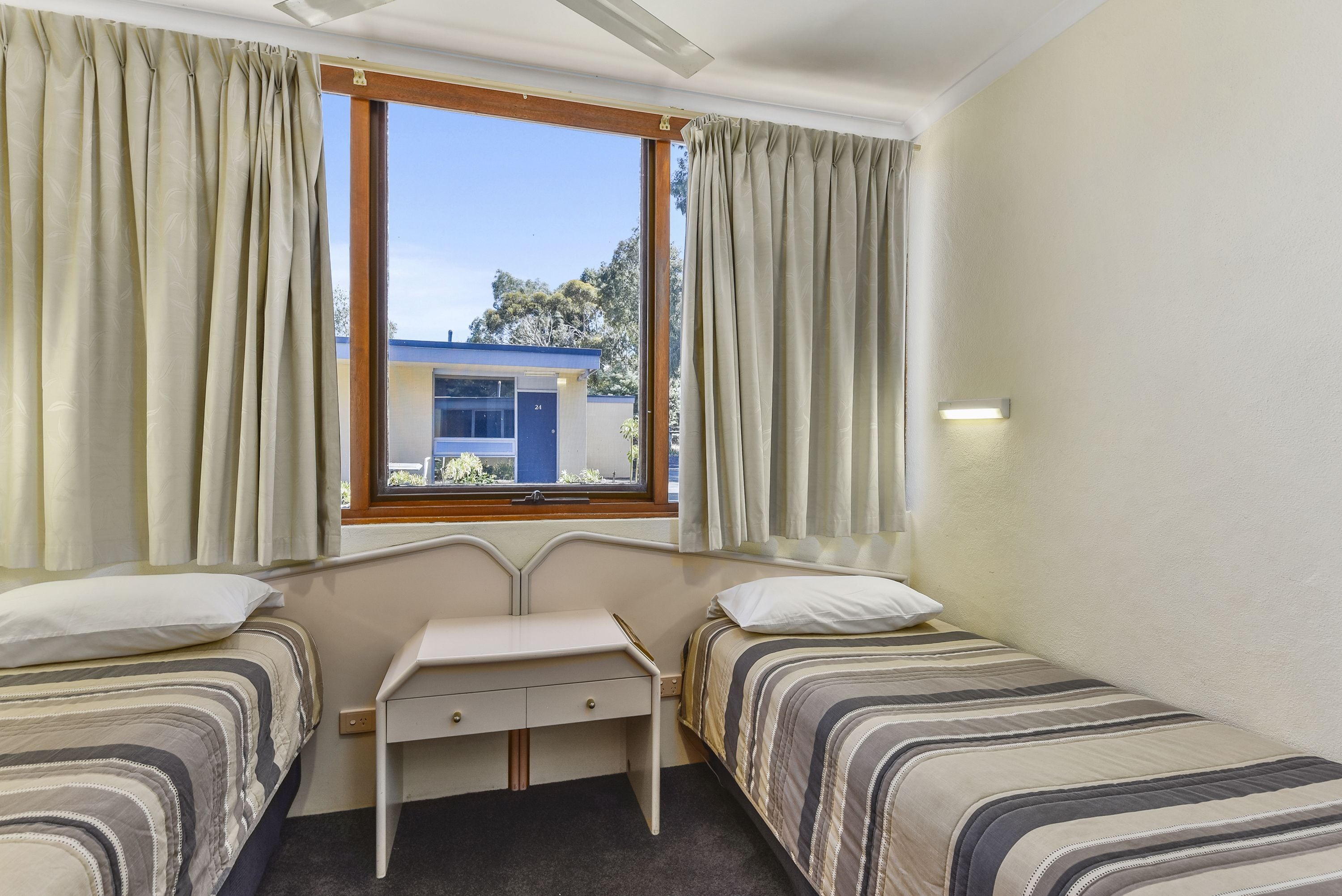 Una habitación con dos camas, un escritorio pequeño y una ventana con cortinas.