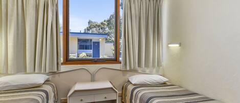 Una habitación con dos camas, un escritorio pequeño y una ventana con cortinas.