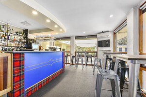 Zona de bar con mostrador azul, estanterías con botellas y un televisor.