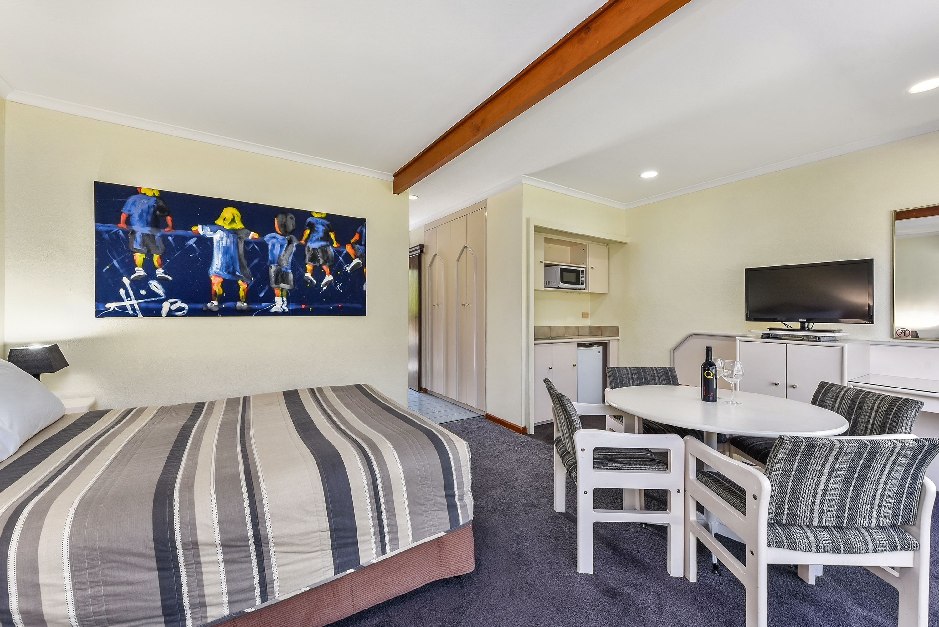 A hotel room with a bed, a dining table with chairs, a TV, and a painting on the wall.