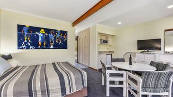 A hotel room with a bed, a dining table with chairs, a TV, and a painting on the wall.