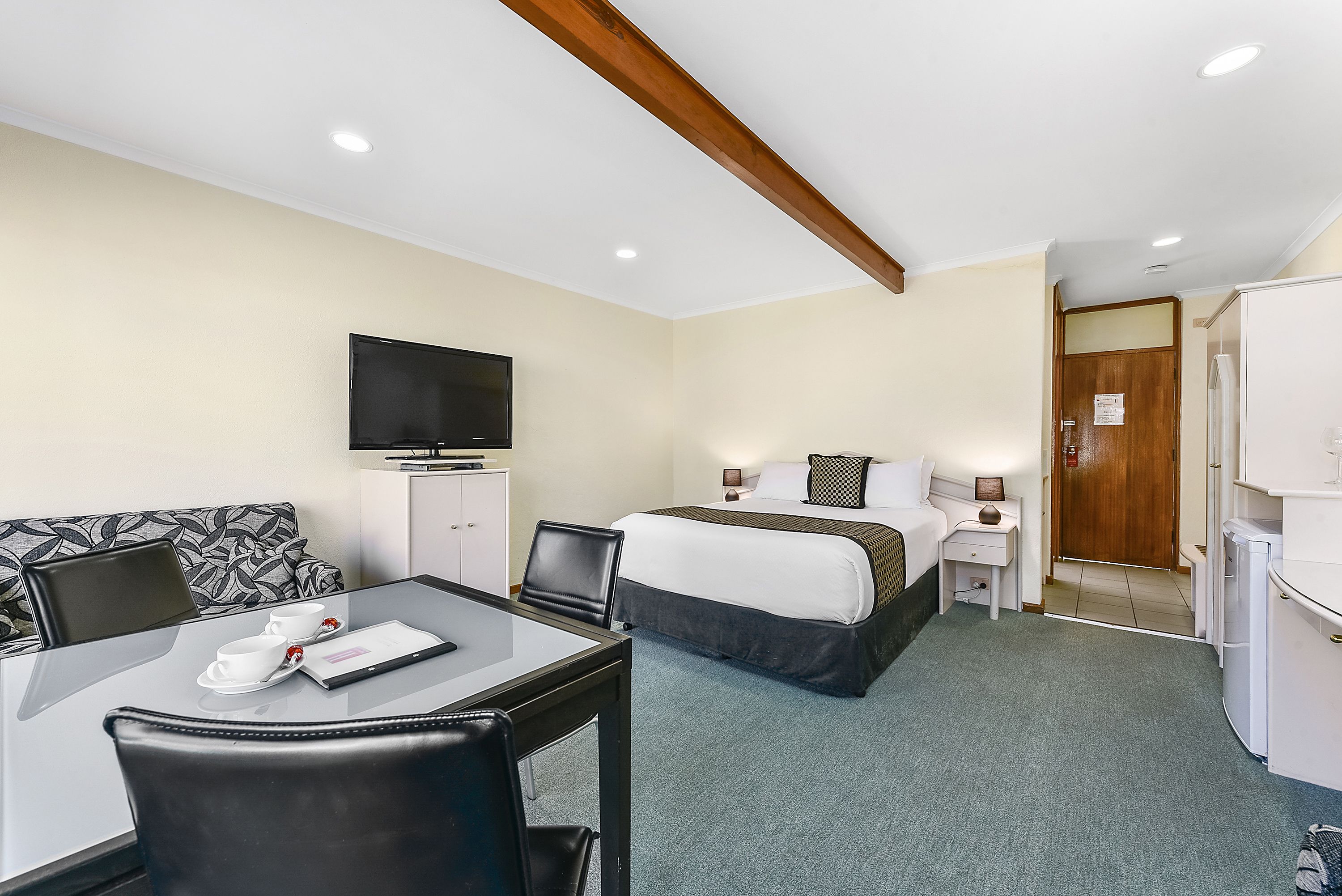 A hotel room with a bed, a desk with a chair, a television, and a small table with cups and a menu.