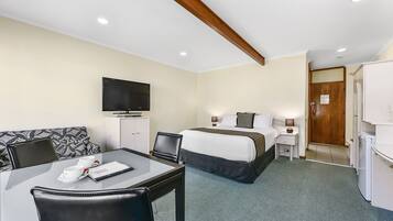 A hotel room with a bed, a desk with a chair, a television, and a small table with cups and a menu.