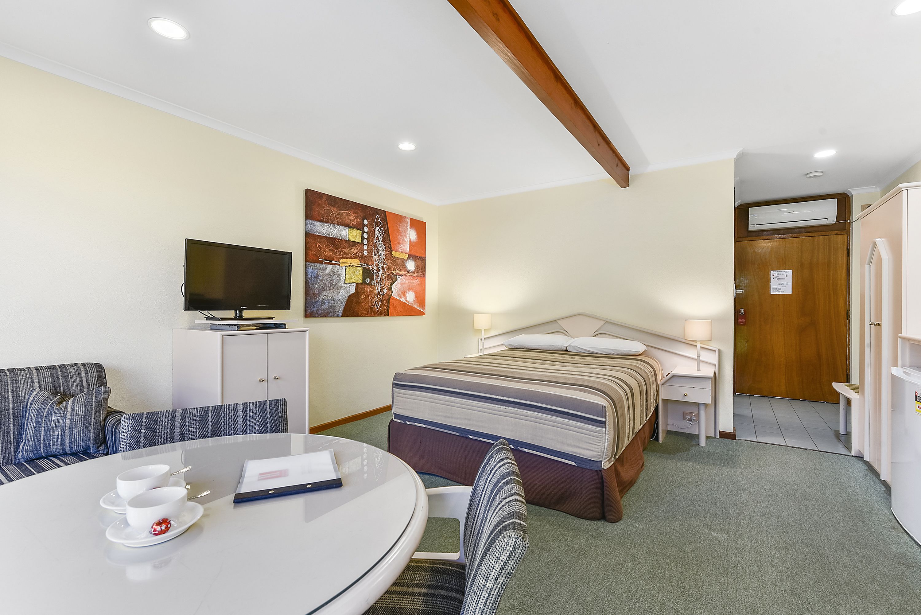 A hotel room with a bed, a TV, a dining table with cups, a sofa, and a painting on the wall.