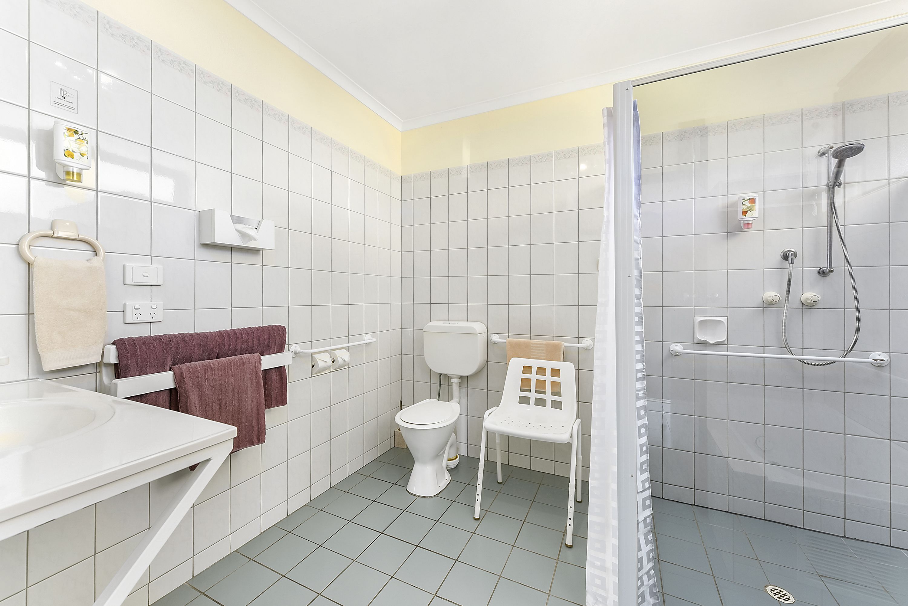 A bathroom with a toilet, a shower, a sink, and a chair.