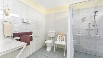 A bathroom with a toilet, a shower, a sink, and a chair.