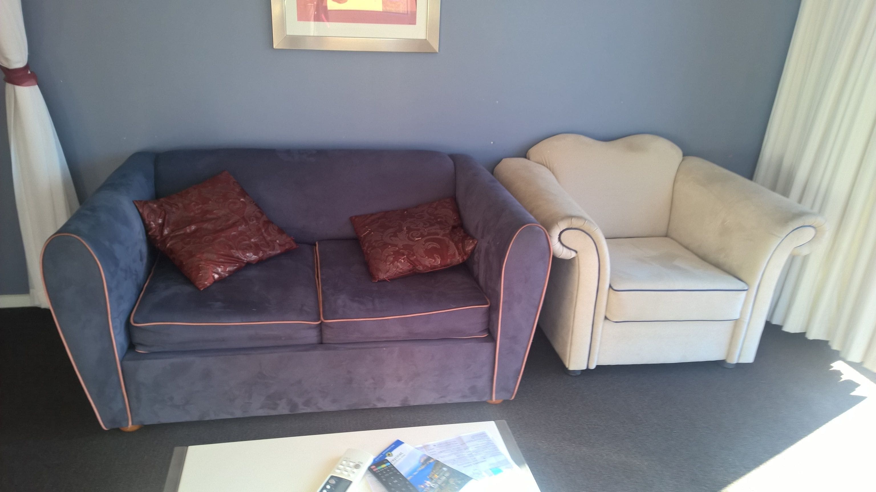 Una habitación con un sofá azul oscuro con detalles naranja, dos cojines a juego y un sillón color beige.