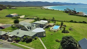 Une grande maison avec une piscine, entourée d’une pelouse bien entretenue et offrant une vue sur l’océan.