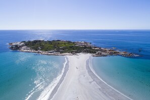 An aerial view of a beach with a small island, clear blue waters, and a sandy shoreline. - Diamond Island Resort & Penguin viewing (Bicheno)