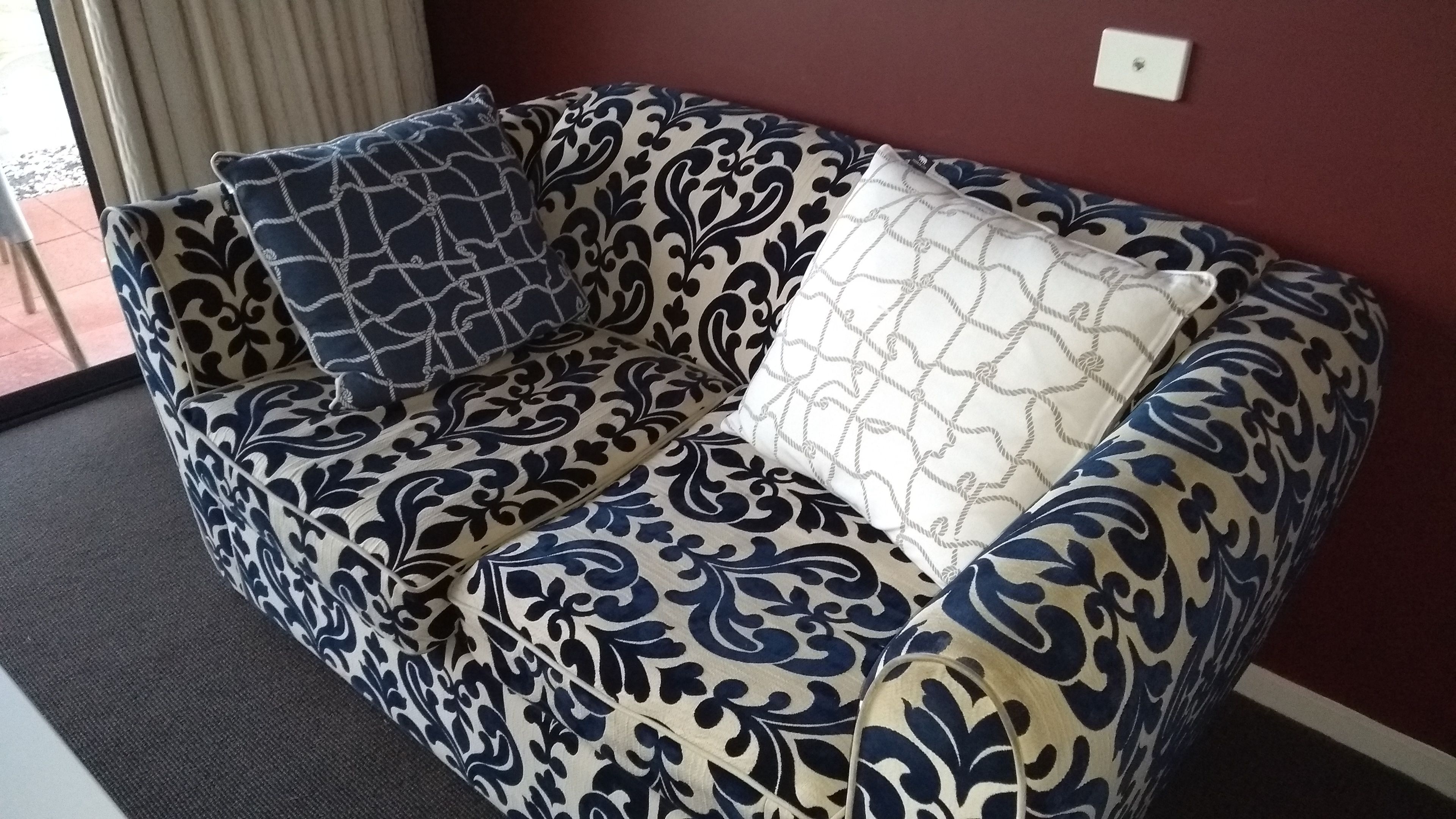 A sofa with a blue and white pattern, two pillows, and a red wall.