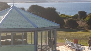 Un belvédère doté d’une structure en verre, d’un espace salon extérieur et offrant une vue sur une étendue d’eau et des collines lointaines.
