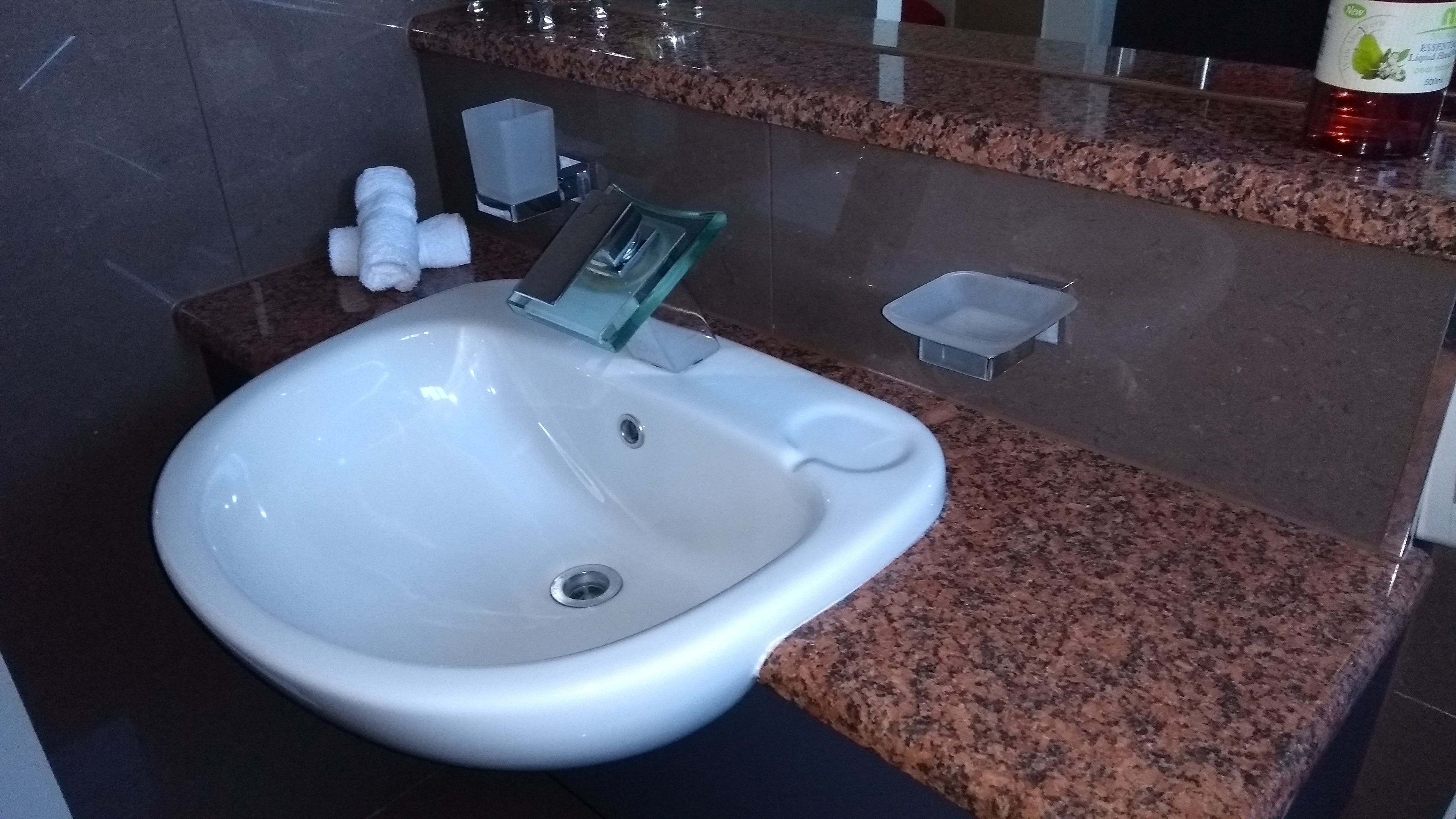 A white sink with a modern design, a granite countertop, and a mirror above it.