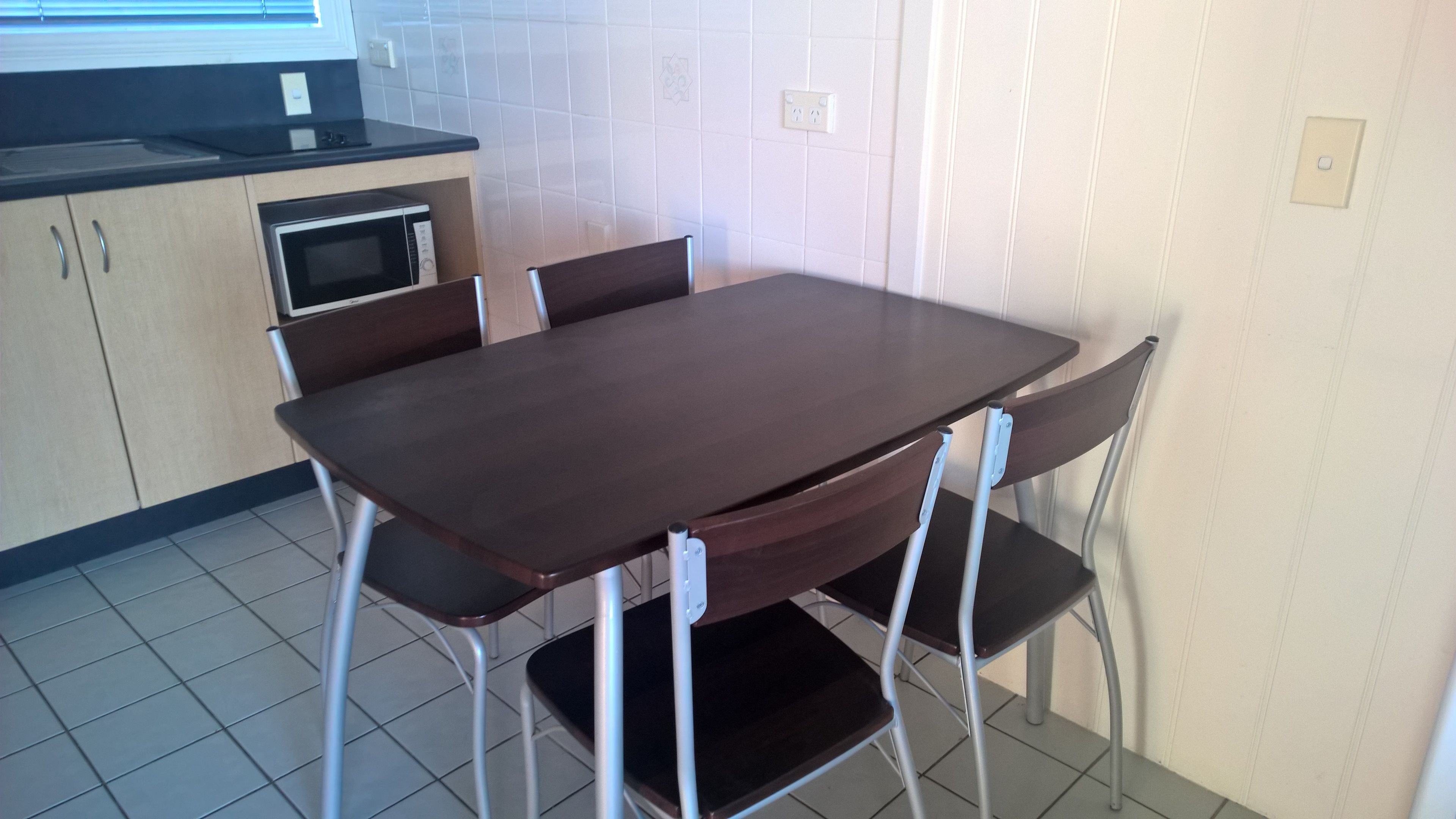 Ett kompakt kök med ett mörkt träbord och fyra stolar, en mikrovågsugn och en liten arbetsbänk.