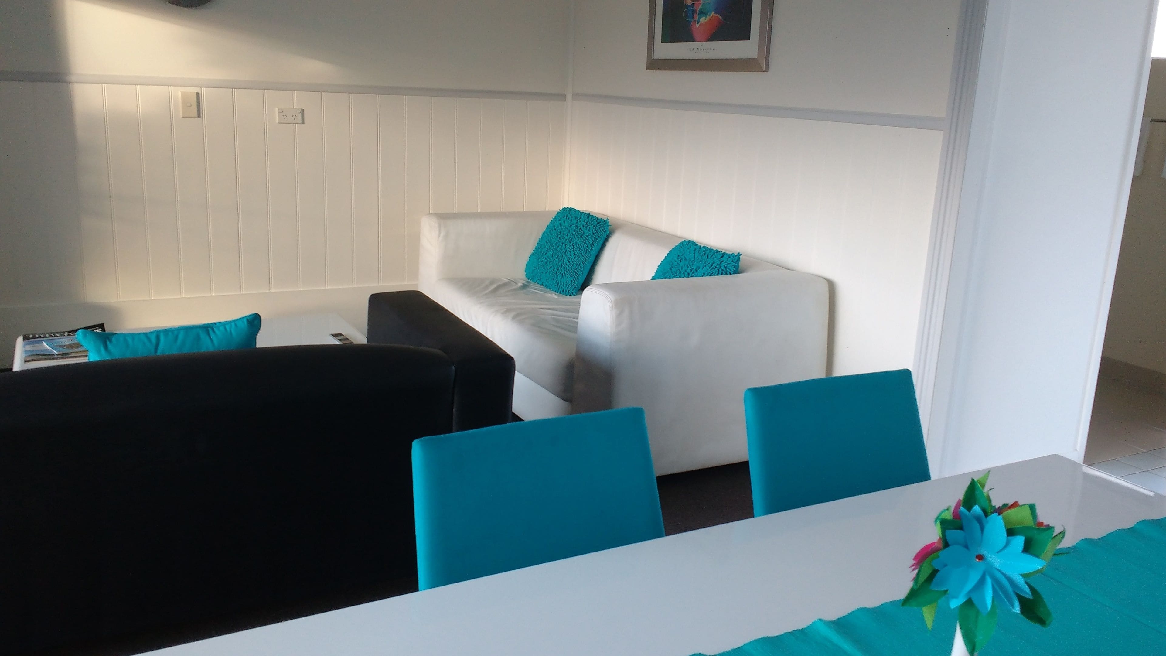 Una habitación con un sofá blanco, sillas negras y azules, y una mesa con mantel color turquesa.