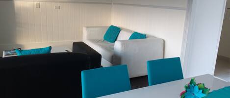 A room with a white sofa, black and blue chairs, and a white table with a teal tablecloth.