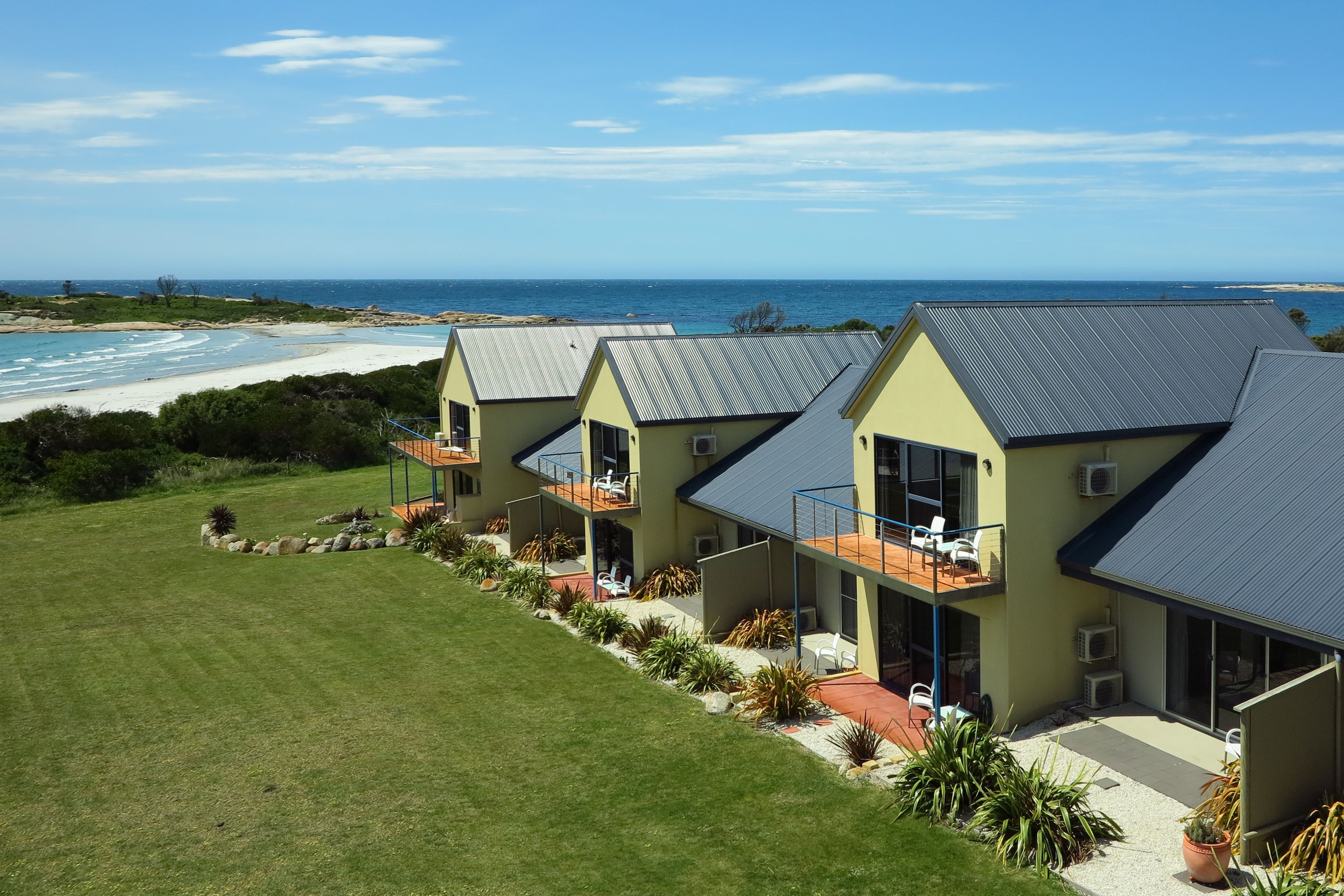 A row of modern, two-story buildings with balconies overlooking a beach.