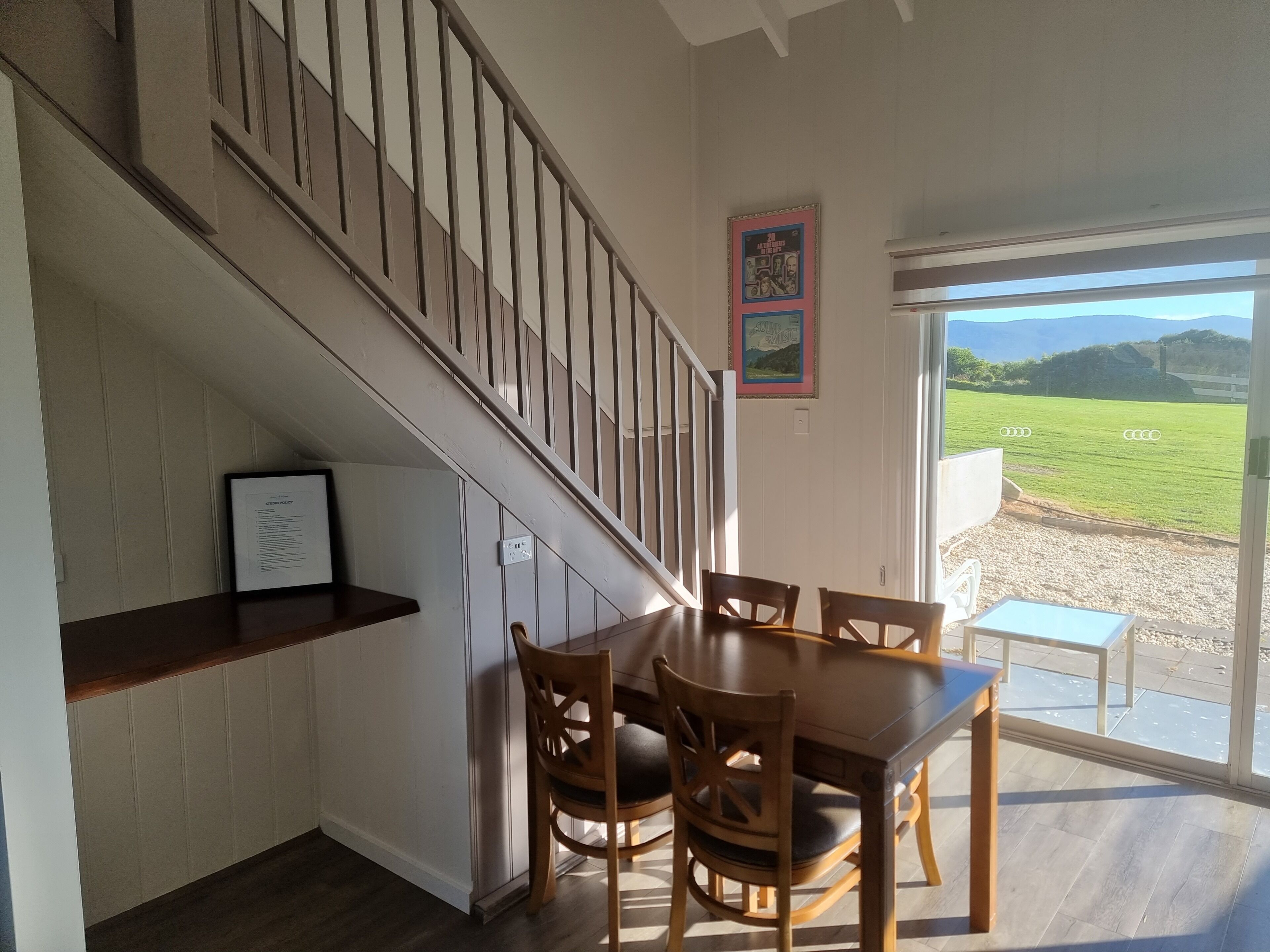 A dining area with a wooden table and chairs, a staircase, and a view of a green field through a glass door.