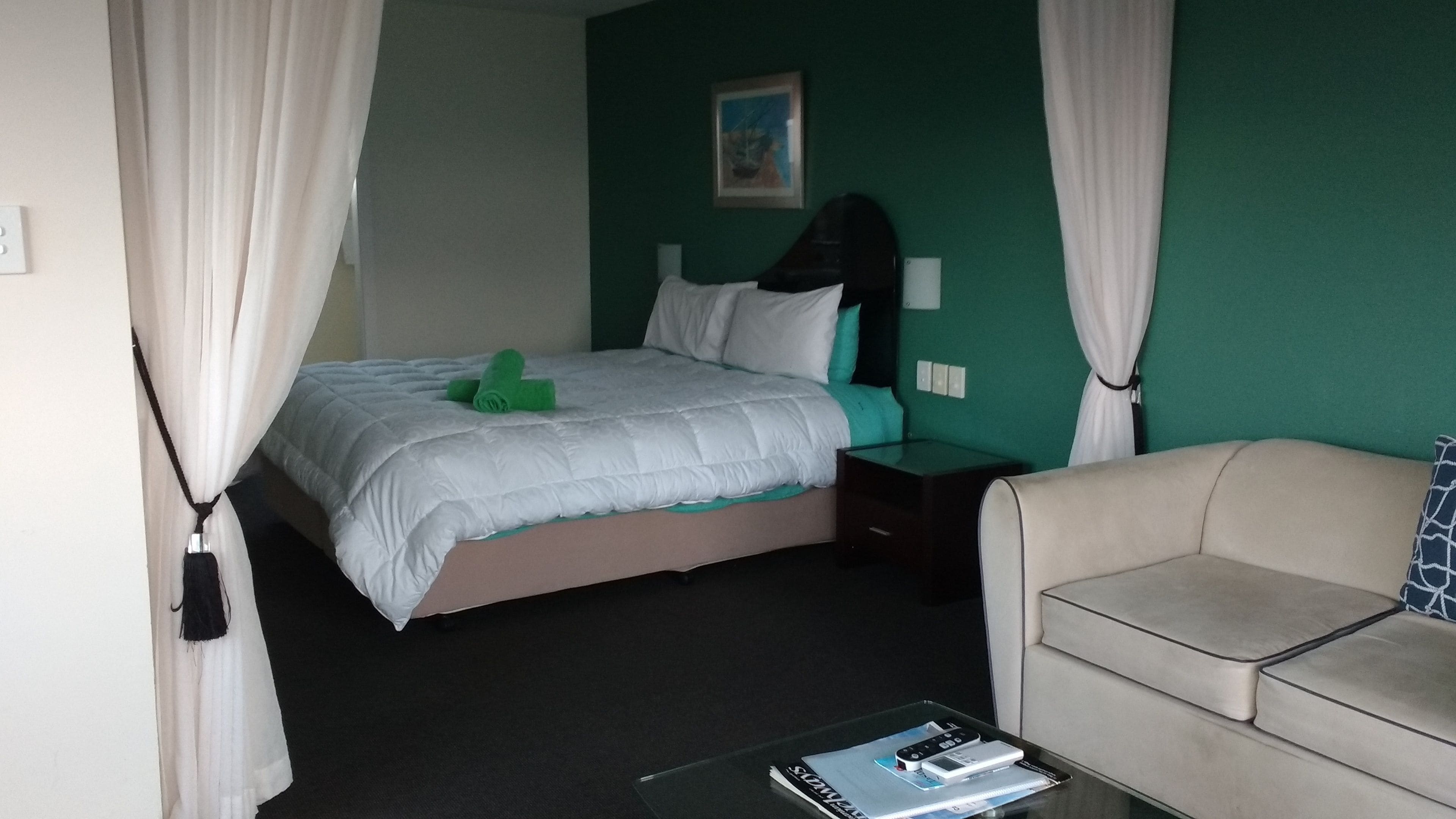 Habitación de hotel con una cama, una mesita de noche, un sofá y una mesa con una revista.
