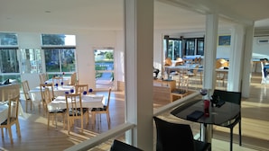 Un vaste espace dédié à la salle à manger, avec de nombreuses tables et chaises, de grandes fenêtres offrant une vue sur l’extérieur et un aménagement intérieur moderne.