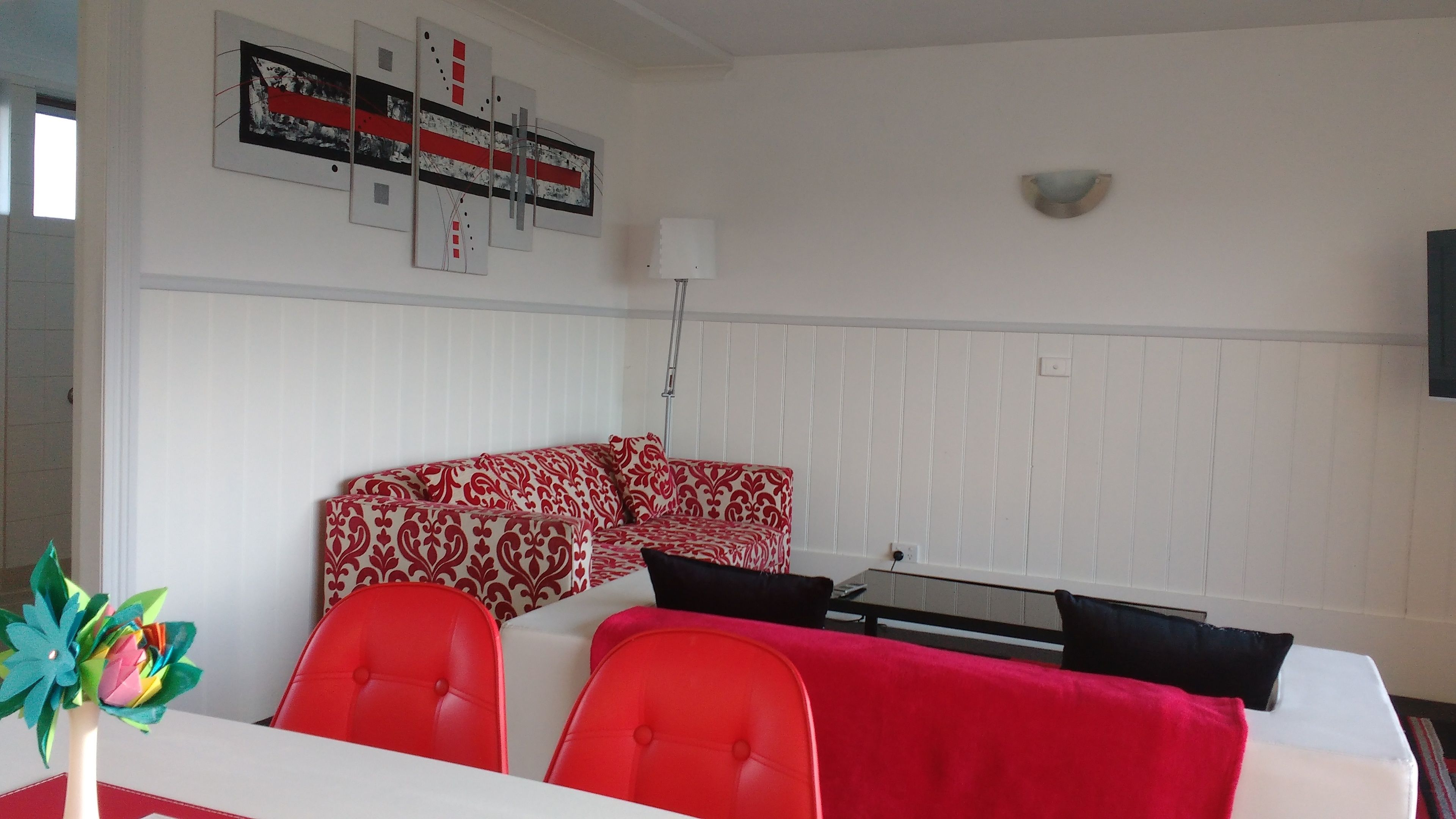 A modern living room with a red and white patterned sofa, a glass coffee table, and a white wall with a decorative art piece.