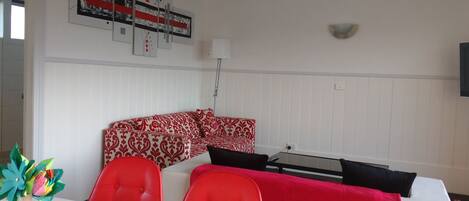 A modern living room with a red and white patterned sofa, a glass coffee table, and a white wall with a decorative art piece.