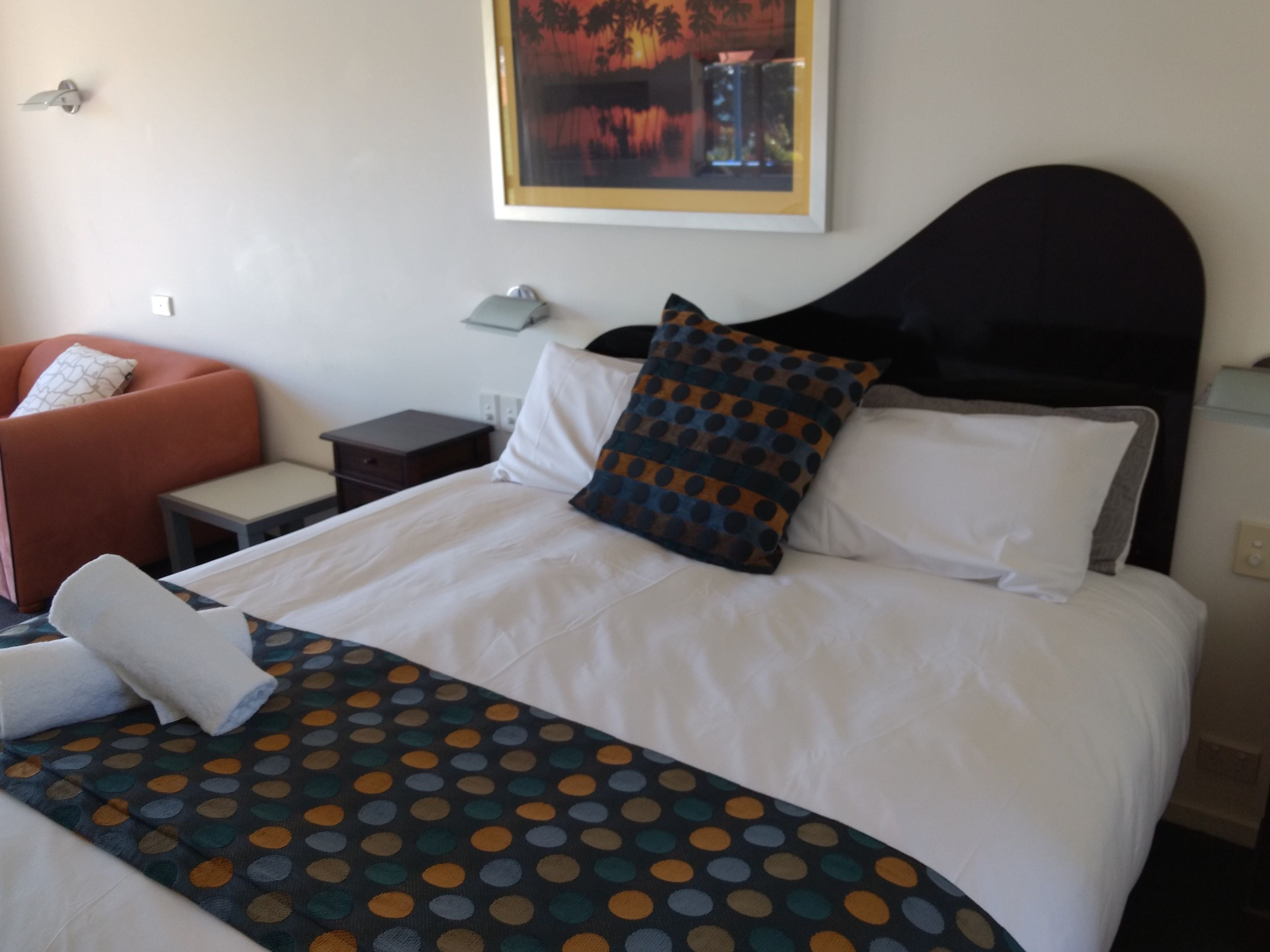 A hotel room with a bed, a nightstand, a chair, and a painting on the wall.