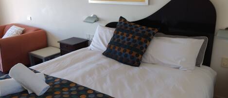 A hotel room with a bed, a nightstand, a chair, and a painting on the wall.