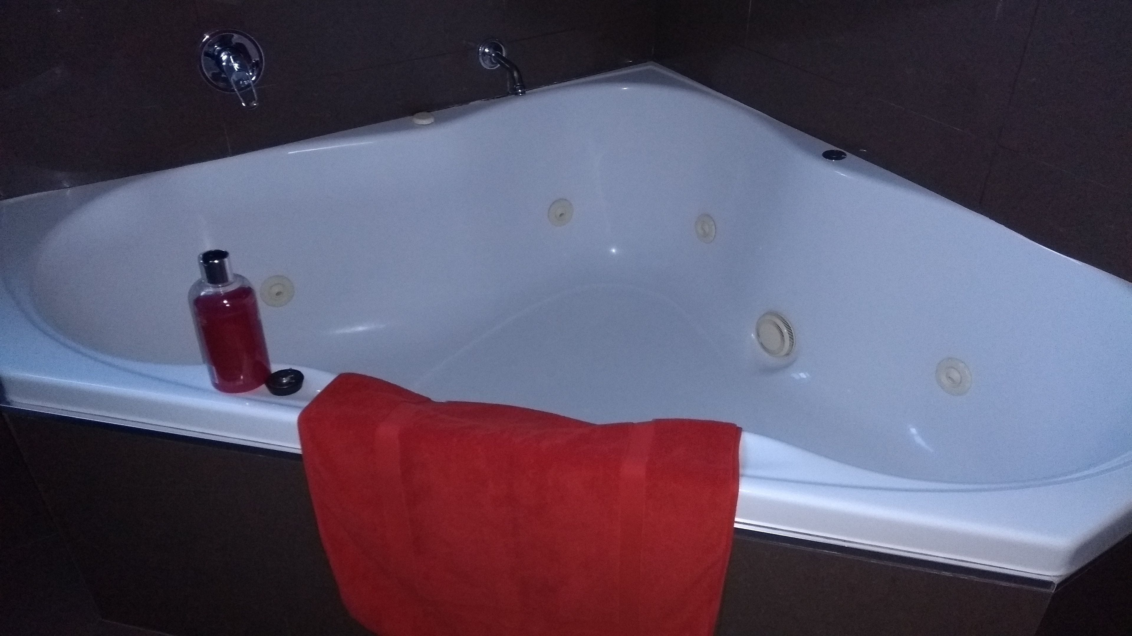 Een wit bad met een rood handdoek, een zeepfles en een kraan.