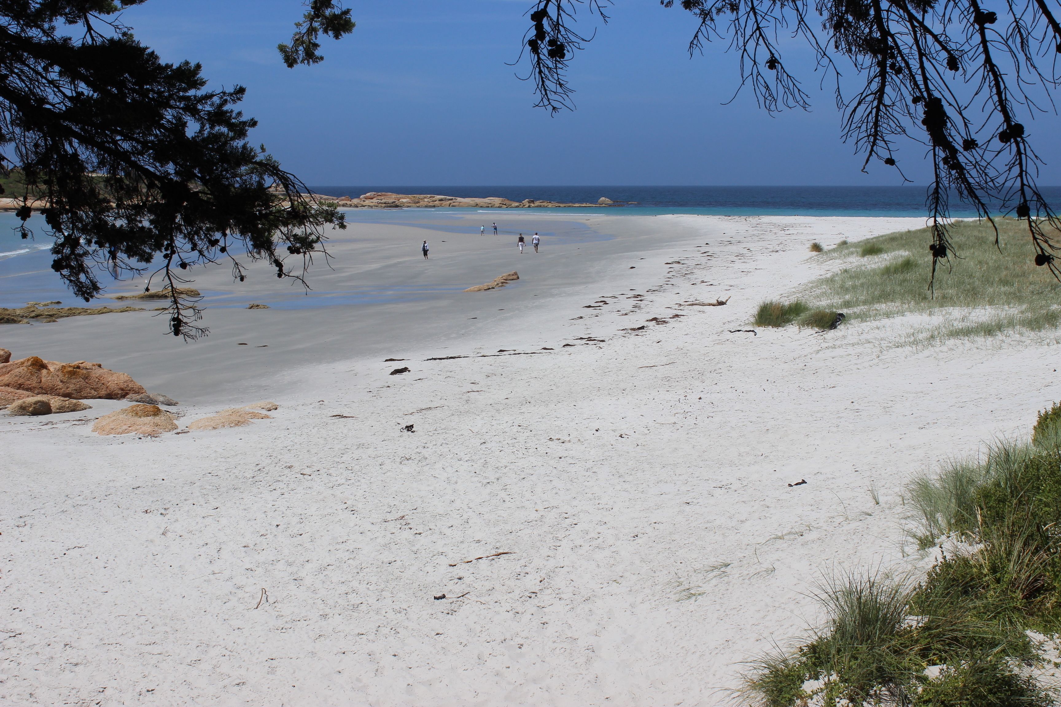 A beach with white sand, clear blue sky, and distant rocky formations.