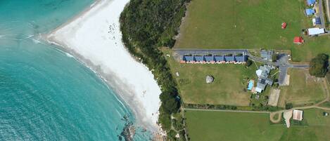 An aerial view of a coastal property with a beach, green fields, and a building complex.