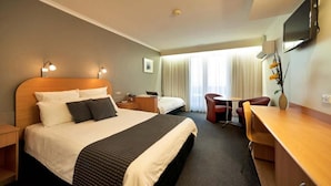 Habitación de hotel con una cama grande, un escritorio, una silla, un televisor y una ventana con cortinas.