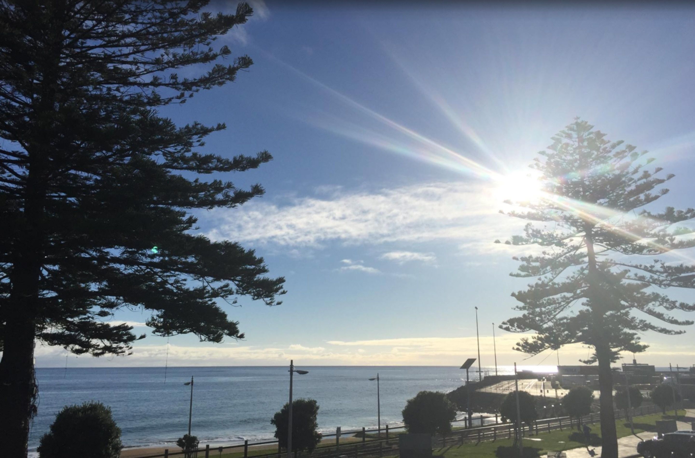 A coastal view with a clear sky, a sun shining through the clouds, and a body of water in the distance.