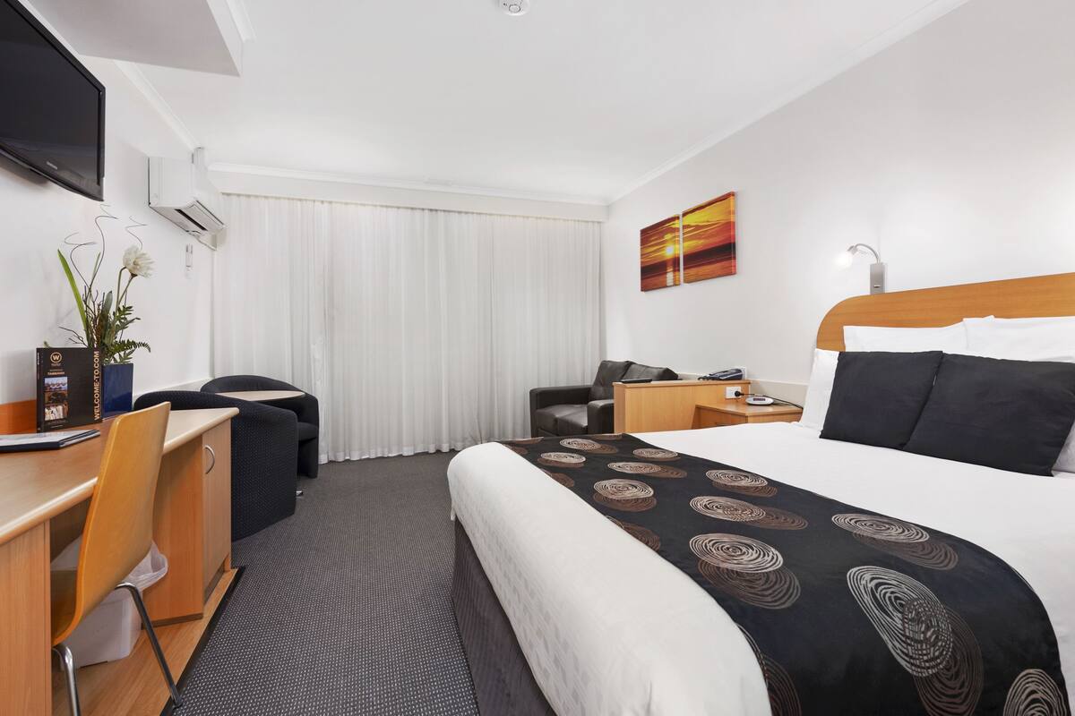 A hotel room with a bed, desk, chair, and a TV.