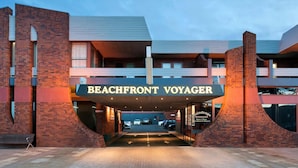 Exterior del hotel Beachfront Voyager, con un letrero llamativo, un acceso cubierto y un área de estacionamiento.