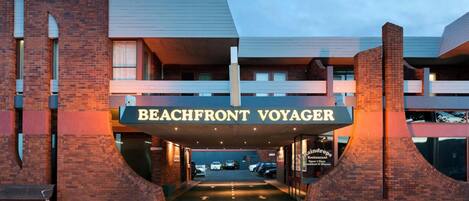 Exterior del hotel Beachfront Voyager, con un letrero llamativo, un acceso cubierto y un área de estacionamiento.