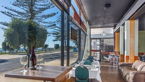 Un restaurante con vistas a la calle y un gran árbol en el exterior. Hay mesas y sillas en su interior.