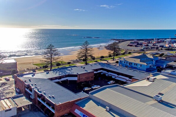 An aerial view of a coastal area with a beach, buildings, and a parking lot. - Beachfront Voyager Motor Inn (Burnie)